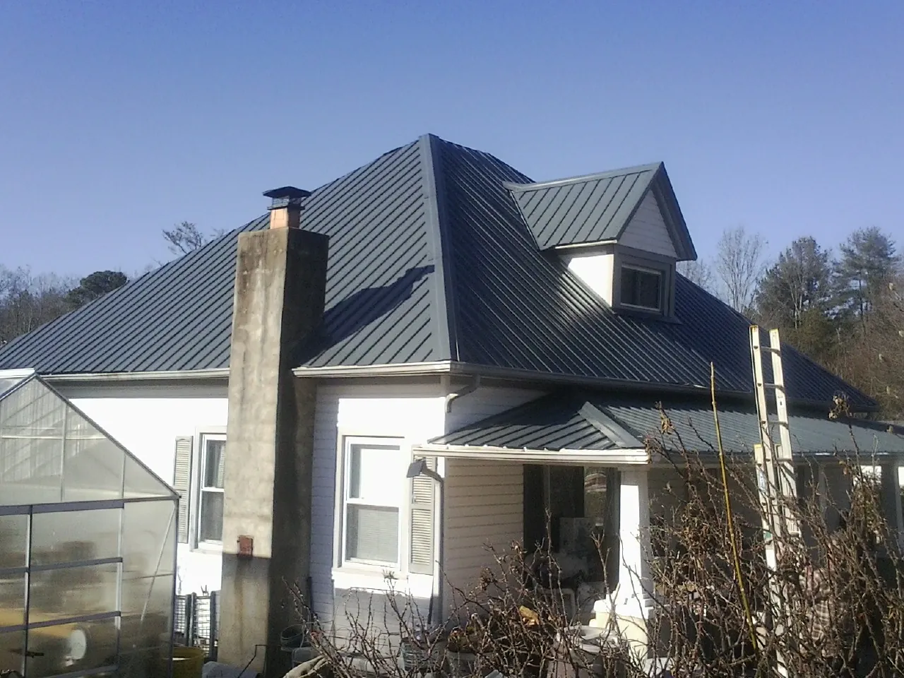Dark blue standing seam metal roof on a white farmhouse with dormer — Slate & Tile Roof Repair by Roofing Brothers in Allenspark