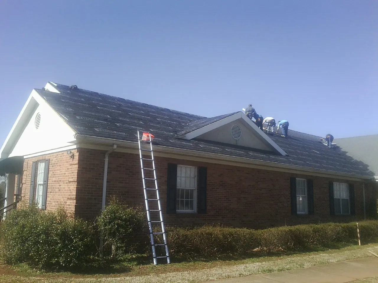 Crew tearing shingles off a brick ranch roof with a ladder set — Emergency Roof Repair work by our crew in Allenspark