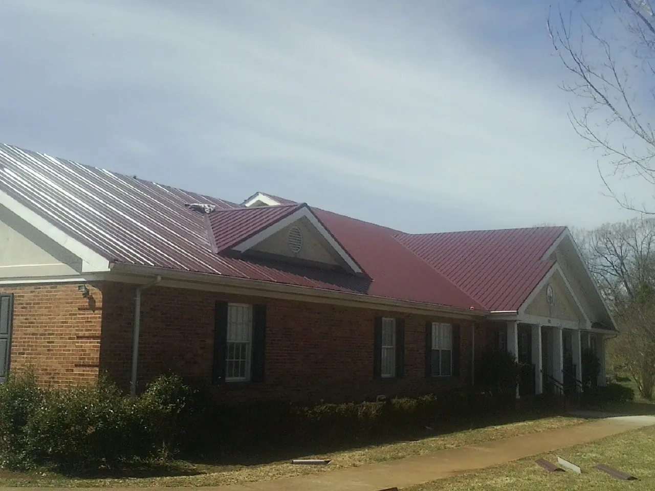 Red metal roof with gabled entries on a long brick building, from a Hail Damage Roof Repair job in Allenspark