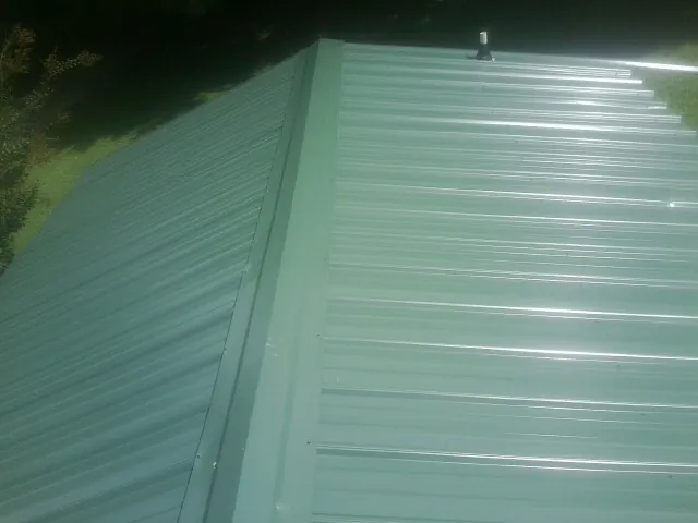 New green metal panels meeting at the ridge of a roof — Flat Roof Repair work by our crew in Allenspark