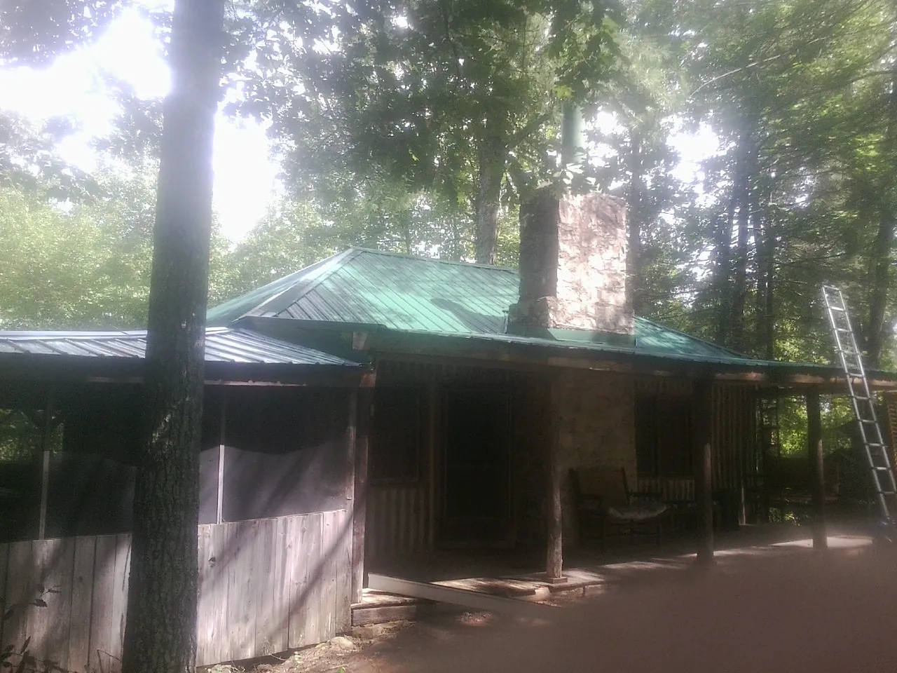Green metal roof and stone chimney above a log cabin porch in Allenspark