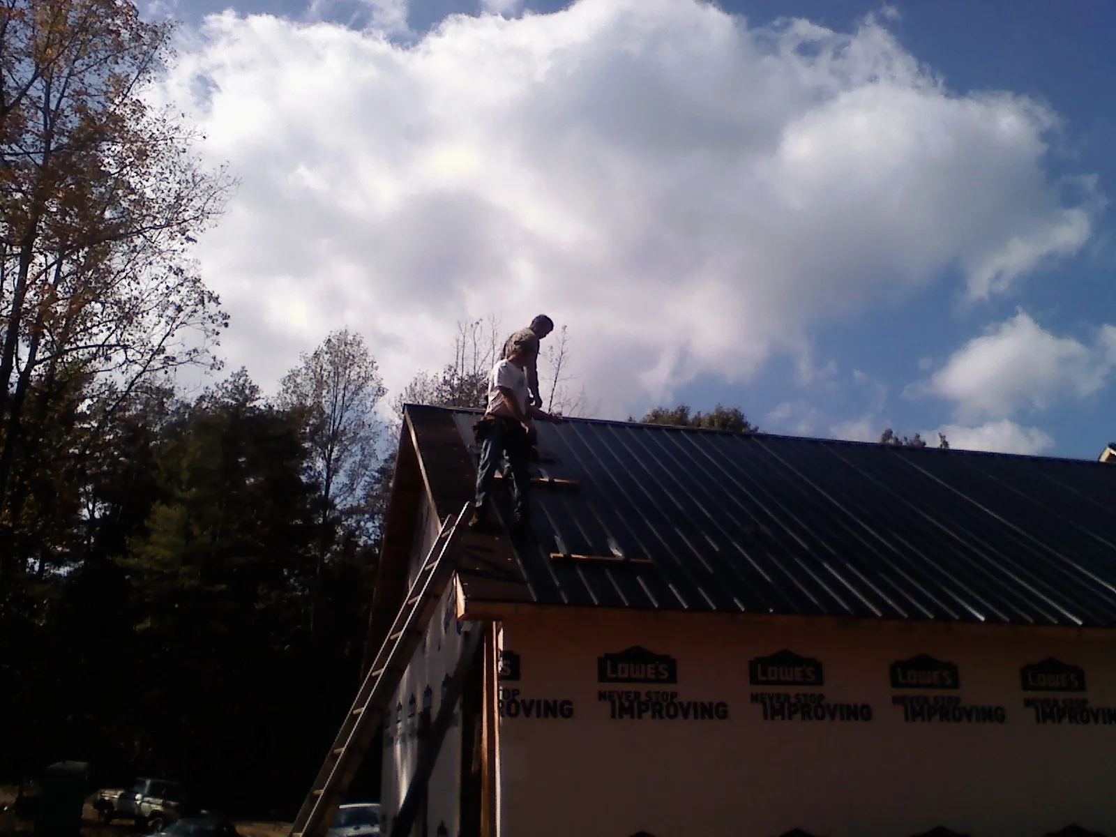 Roofer fastening dark metal panels high against a cloudy sky, from a Roof Inspection job in Allenspark