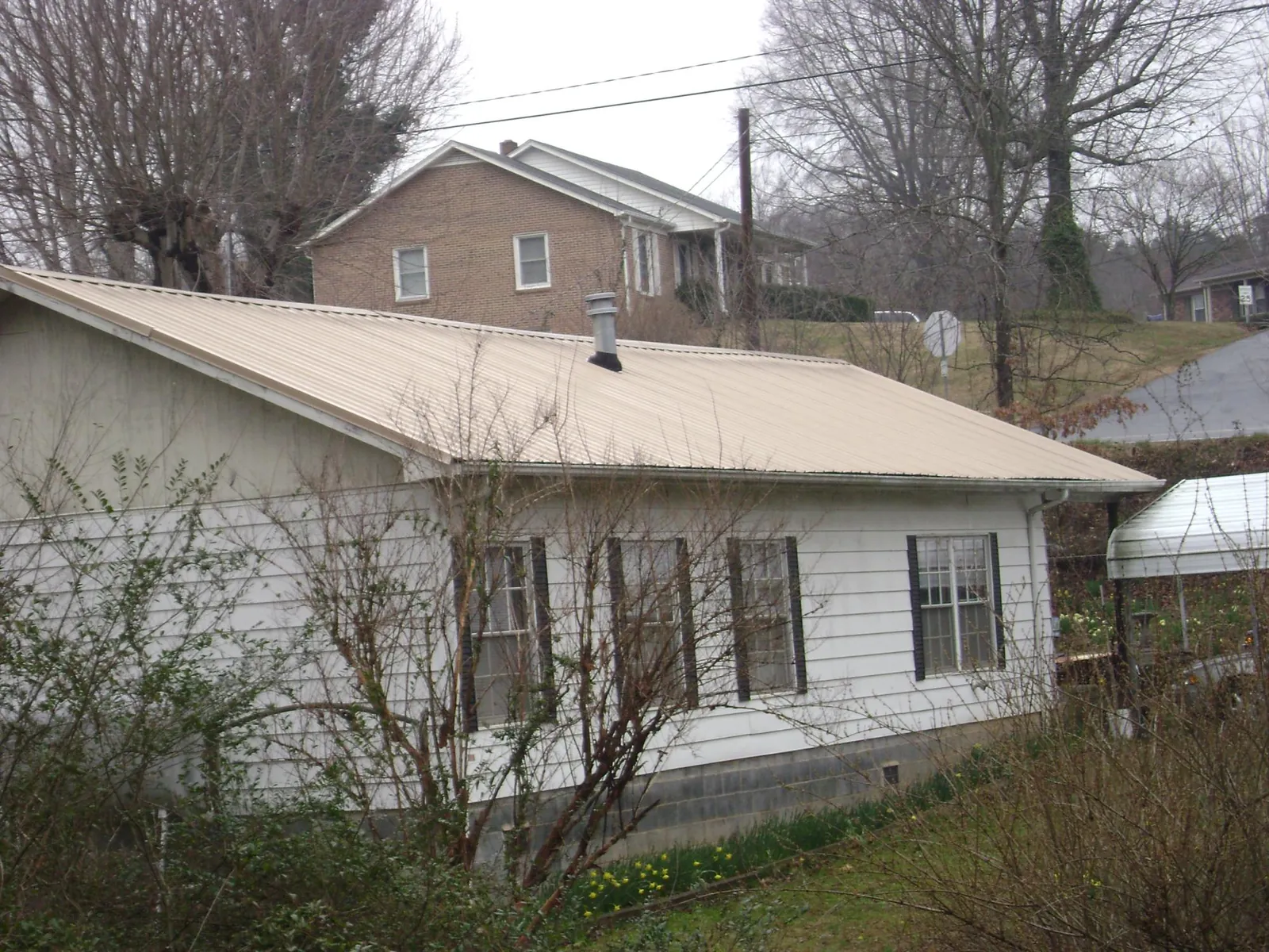 Tan metal roof on a white sided house set into a hillside — Commercial Roofing by Roofing Brothers in Allenspark
